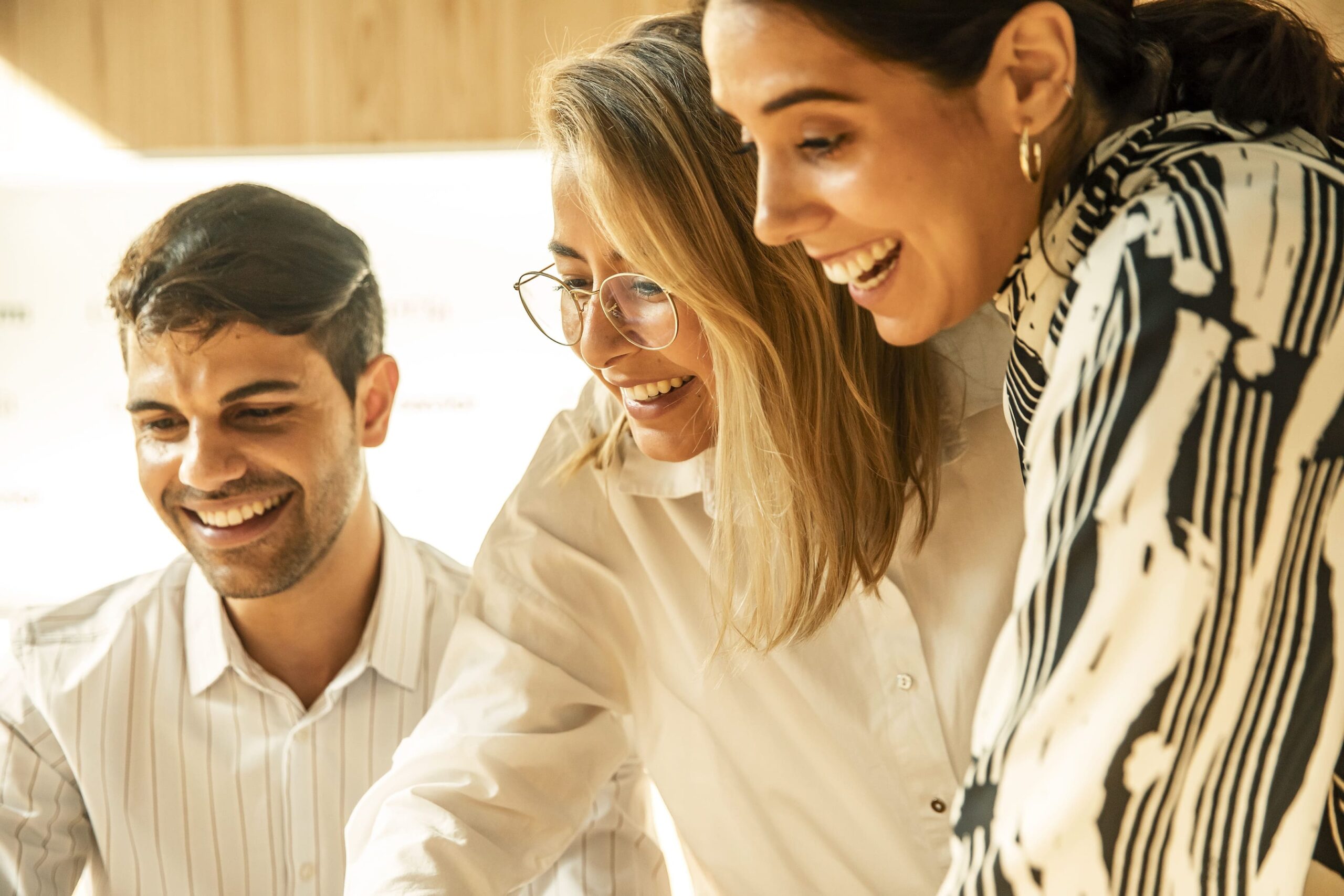 Três profissionais a sorrir em ambiente de trabalho colaborativo - liderança e trabalho em equipa