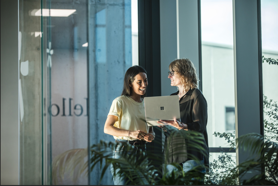 Duas pessoas colaboram num escritório moderno, analisando informação num portátil.