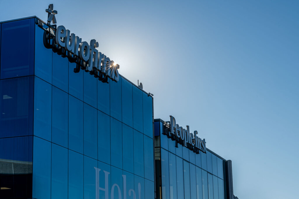 Fachada envidraçada do edifício Eurofirms com logotipo visível e céu azul ao fundo.