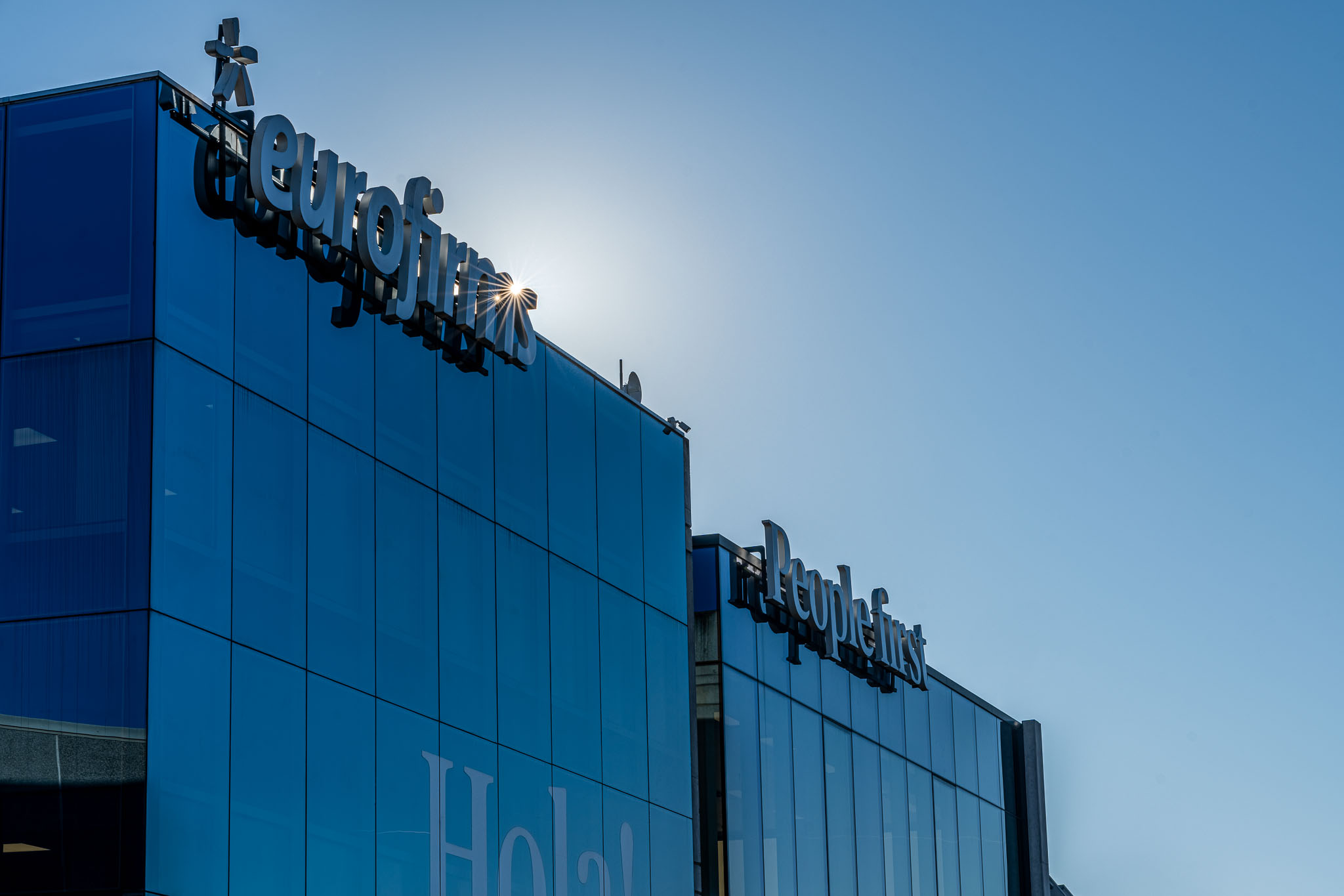 Fachada envidraçada do edifício Eurofirms com logotipo visível e céu azul ao fundo.