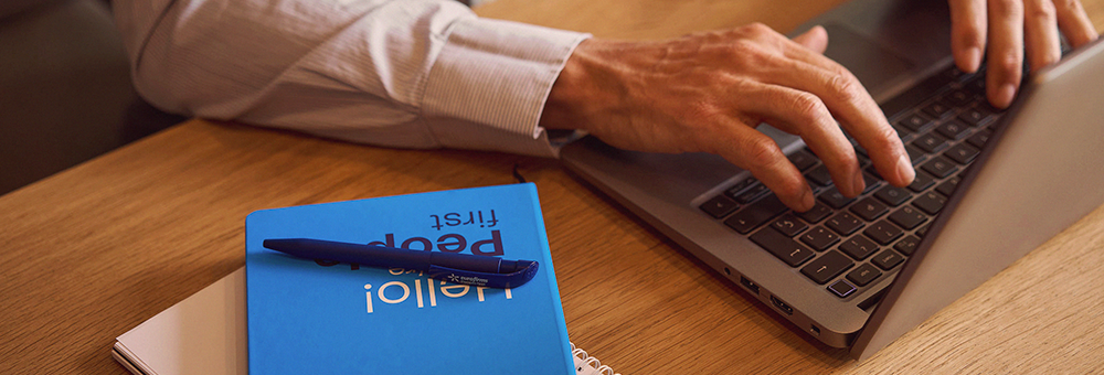 Mãos a escrever num portátil ao lado de um caderno Eurofirms com a mensagem People First, representando segurança e confiança nas comunicações digitais.