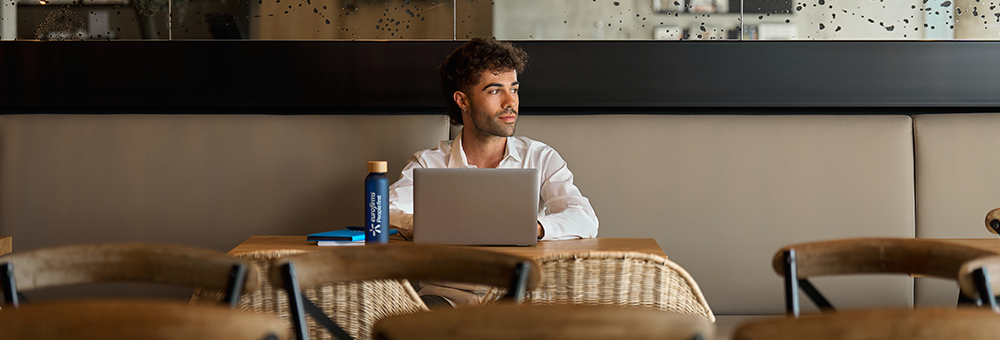 Pessoa a trabalhar num portátil numa mesa de café, com garrafa reutilizável e caderno ao lado.