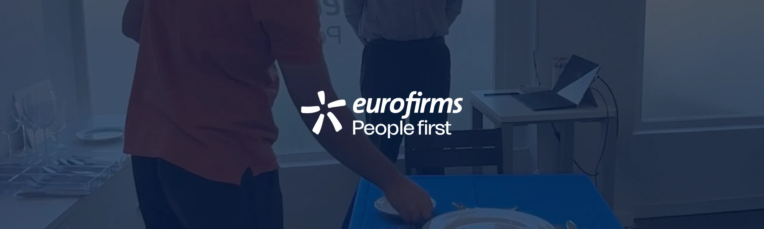 A imagem demonstra uma formação do programa de competências básicas da Eurofirms a decorrer no fundo, sobrepondo-se o logo da Eurofirms a branco, sobre um fundo azul escuro.